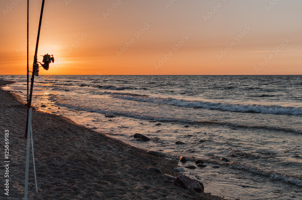 Sunset over the sea. Stones and fishing rods on the foreground Sunset over the sea. Stones and fishing rods on the foreground