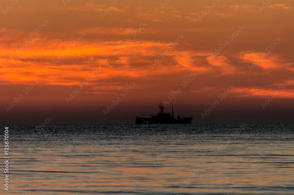 Sunrise at sea shore. Colorful sky and clouds. Army ship.