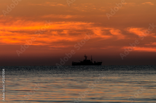 Sunrise at sea shore. Colorful sky and clouds. Army ship. © Kazick