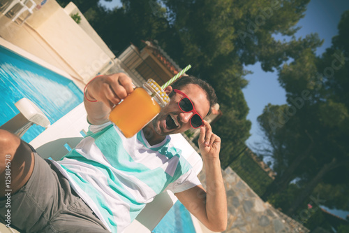 Young man on the swimming pool holding jar with orange juice.     © Kitja