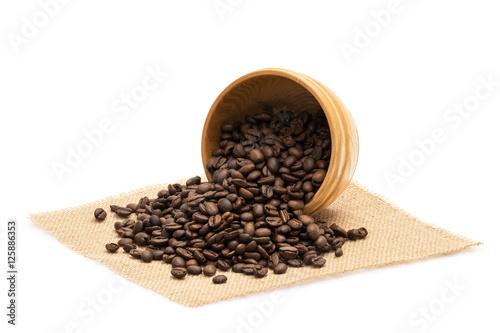 Roasted coffee beans with an overturned wooden bowl on a piece of sack cloth with white background