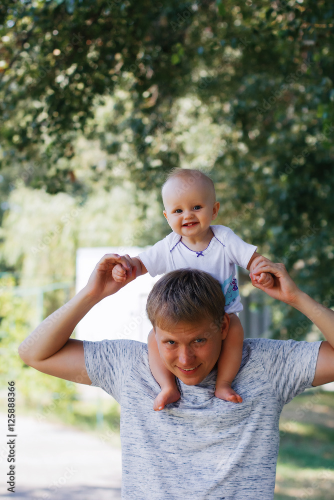 Fototapeta premium Daughter sits on the shoulders of a young father