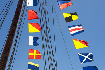 Colorful nautical sailing flags flying in the wind from the lines of a sailboat mast backlit in bright blue sky by the sun