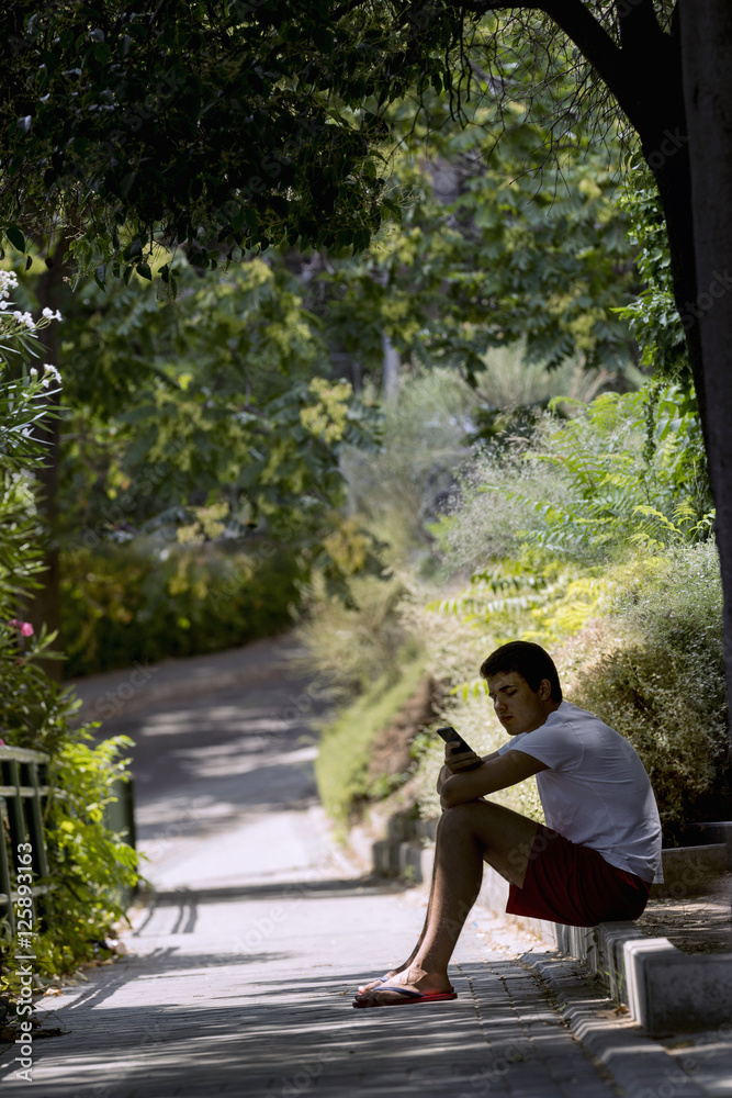 Fototapeta premium Teenager, sitting on a curb, using the mobile phone