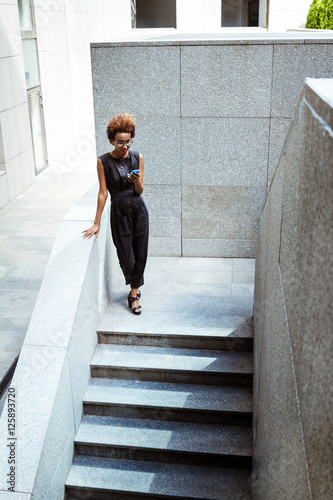 Young beautiful african girl looking at phone going down stairs.