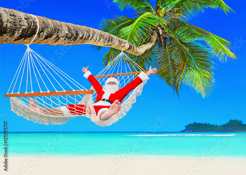 Positive Christmas Santa Claus relax in hammock at palm beach