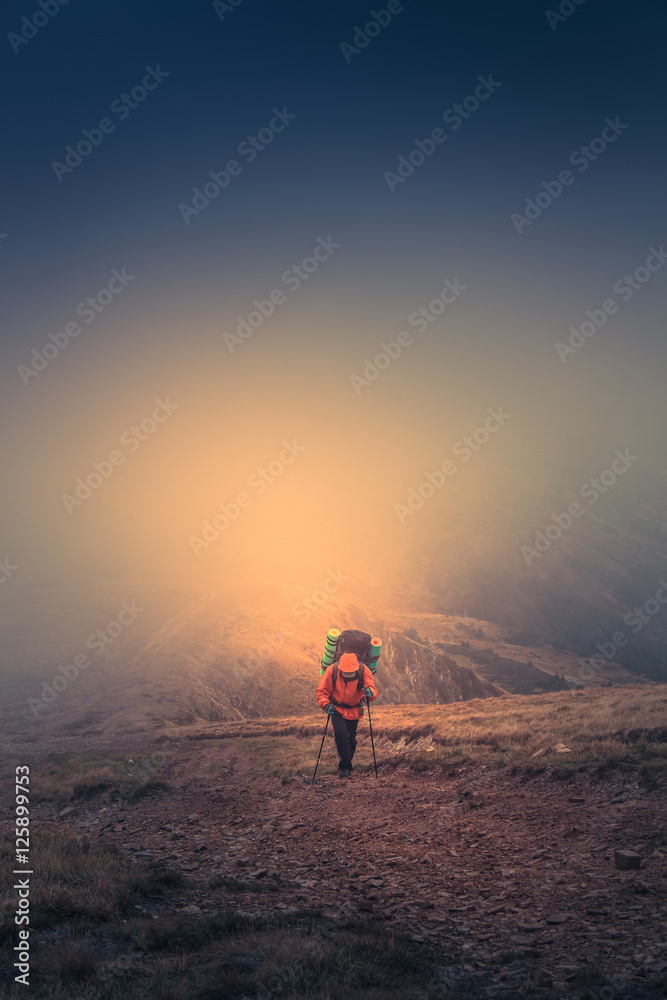 Lonely hiker  with backpack walking along the trail on the mountain top at foggy day time. Travel lifestyle concept.