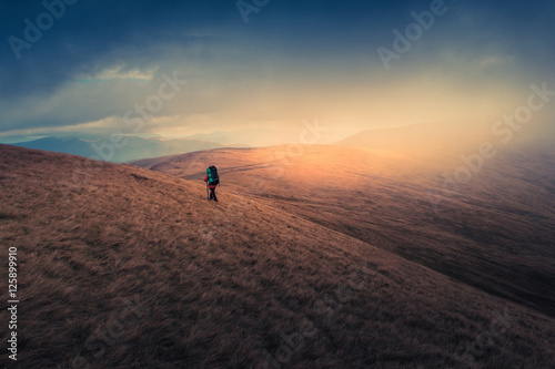 Lonely hiker with backpack walking along the trail on the mountain top at foggy day time. Travel lifestyle concept.