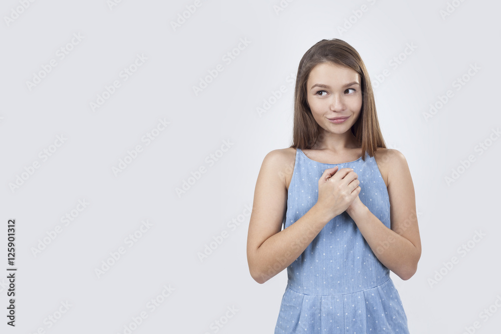 Shy girl in blue dress is standing against gray background Shy girl in blue dress is standing against gray background