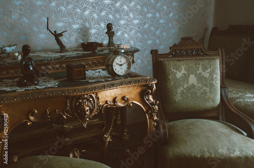 Details of vintage furniture with retro metal winding clock,  armchairs and wooden tables.