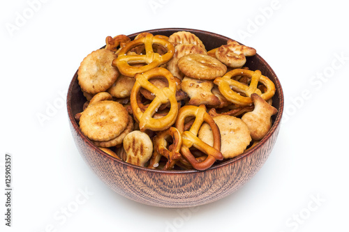 Mix of salty snacks (crackers and pretzels) in wooden bowl isolated on white background