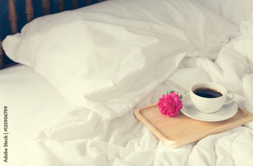 Cup of coffee and pink rose flower with wooden tray on bed backg