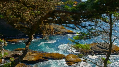 Gliding nature shot of picturesque and mysterious Cape Flattery bay by Pacific ocean coast with rich and colorful blue water, powerful waves and trees on a sunny, warm summer day