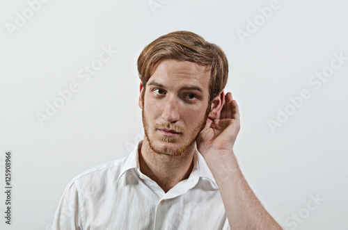 A Young Adult Male Wearing White Shirt with His Hand Near His Ear. Gestures Can Not Hear or Talk Louder.