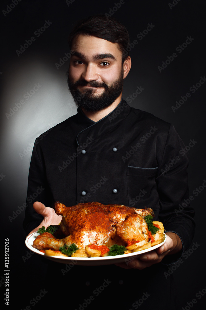 Professional chef with a beard in black uniforms with cooked chicken in his hands Professional chef with a beard in black uniforms with cooked chicken in his hands