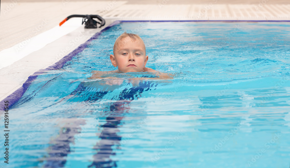 A blond boy learning to swim in a swimming pool