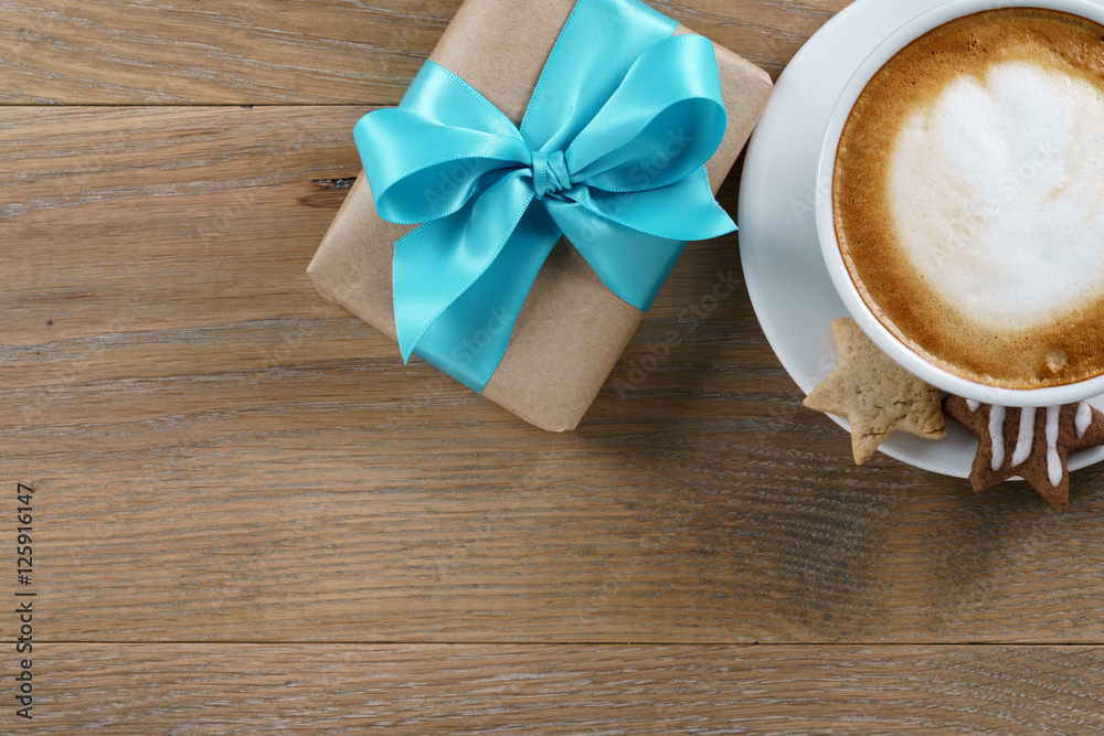 cup of cappuccino and gift box with azure ribbon on wooden oak table top view