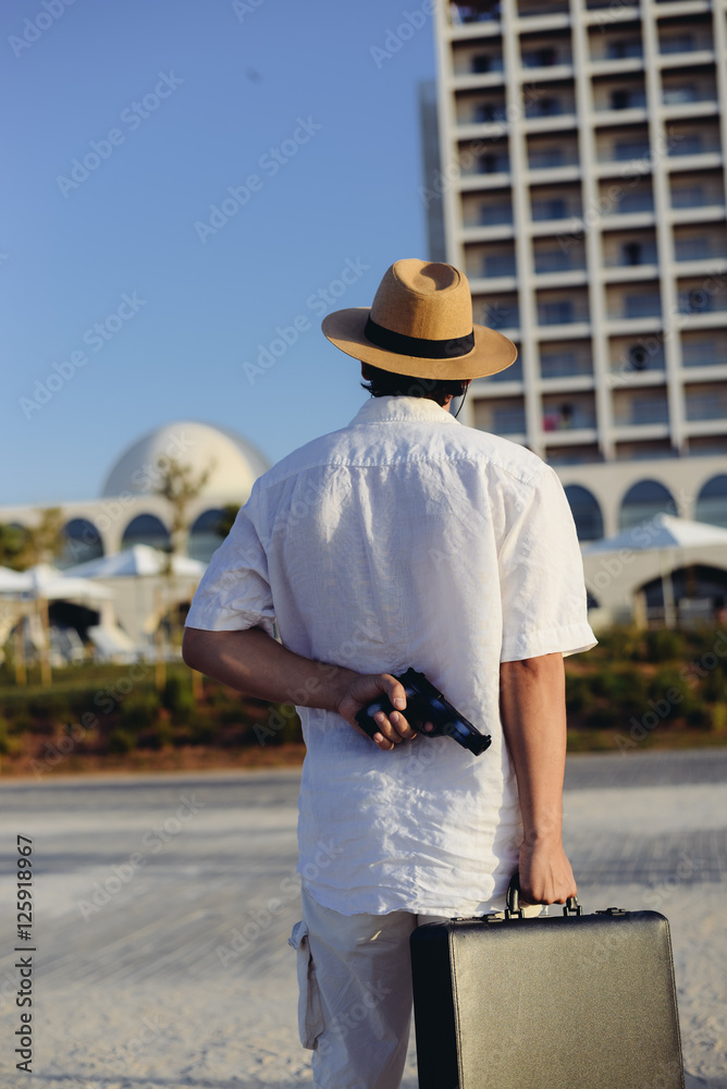 Rear view of man holding gun and briefcase on sunny outdoors background