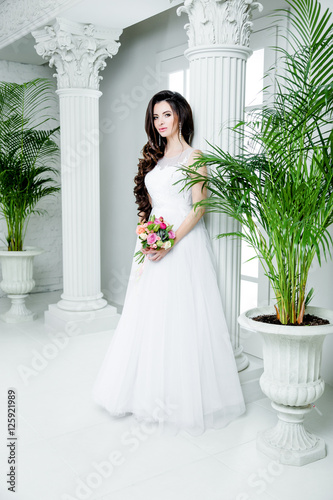 gorgeous bride in luxury wedding dress. Bride. Perfect Make up and Long Wavy Hair. Hairstyle, wedding jewelry. Beautiful Woman with Shiny Brown Hair. gorgeous wedding bouquet of various flowers.