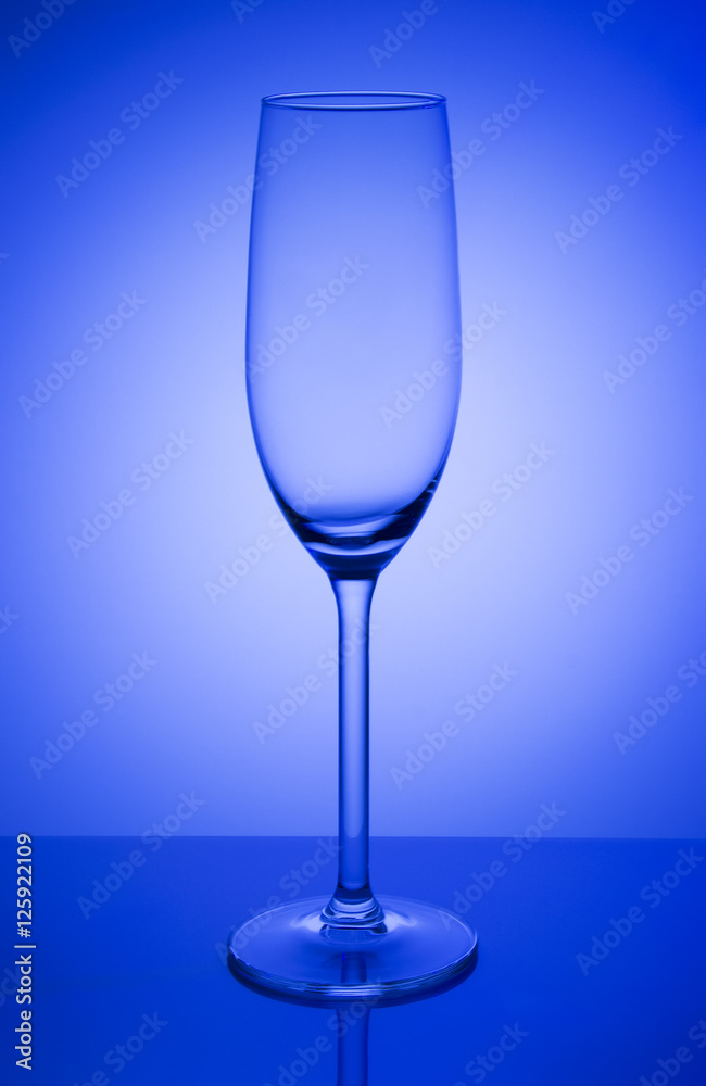 Empty champagne glass on a mirror with spot in blue background Empty champagne glass on a mirror with spot in blue background