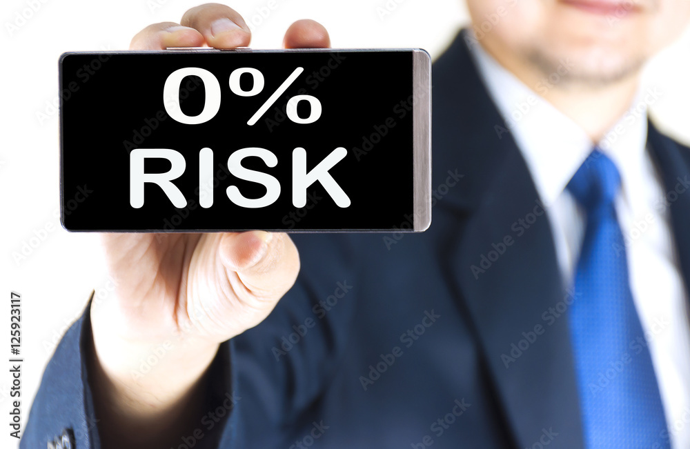 0% RISK word on mobile phone screen in blurred young businessman hand over white background, business concept 0% RISK word on mobile phone screen in blurred young businessman hand over white background, business concept