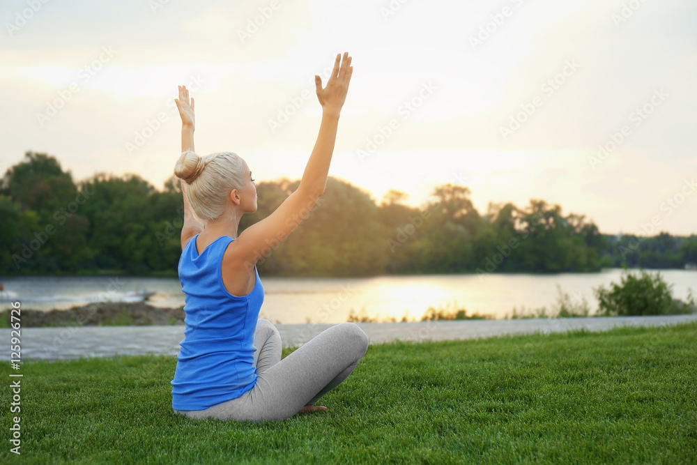 Young woman practicing yoga on grass near pond Young woman practicing yoga on grass near pond