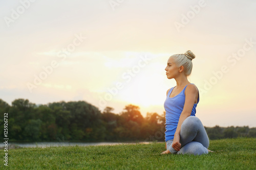 Young beautiful woman practicing yoga while sitting on grass