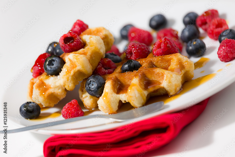Close-up of waffles with berries and maple syrup on a white plat