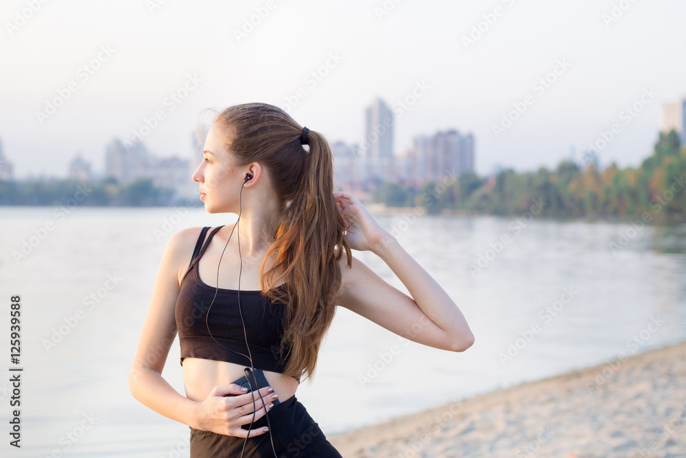 Fitness woman at river listening to music on mobile phone