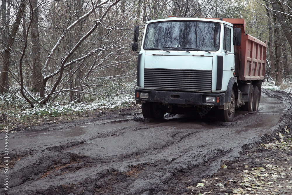 Truck going on the rutted road through the autumn forest