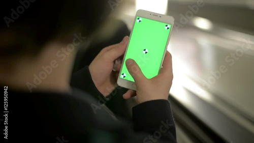 Close up of hand using a smartphone with green screen display at underground train station.