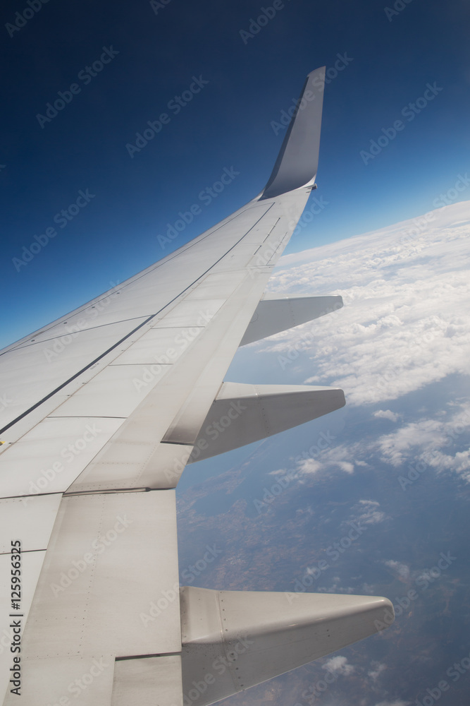 Wing of an airplane flying above the clouds. people look at the sky from the window of the plane, using air transport to travel. back light sun beam Wing of an airplane flying above the clouds. people look at the sky from the window of the plane, using air transport to travel. back light sun beam