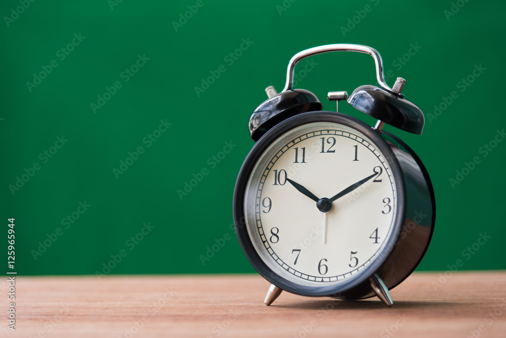 black alarm clock on wooden table with green background black alarm clock on wooden table with green background