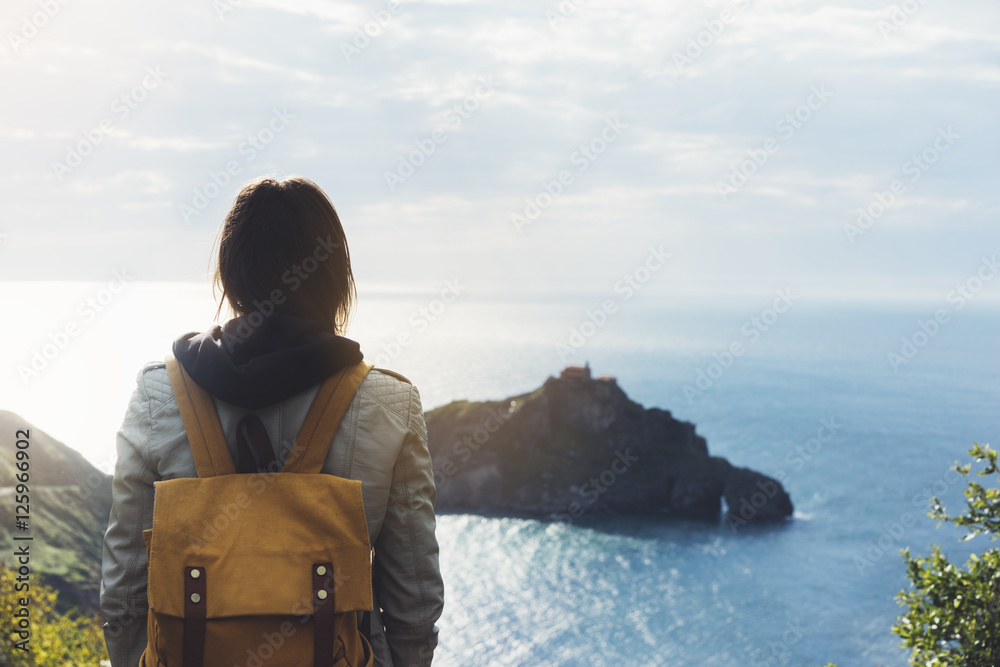 Hipster young girl with backpack enjoying sunset on seascape on peak mountain. Tourist traveler on background valley landscape view mockup. Hiker looking ocean in trip holiday in basque island