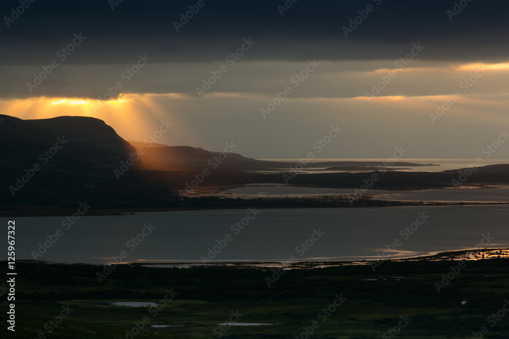 Storm sky with majestic golden rays of  setting sun over  sea. Arctic summer, the tundra, Norway.