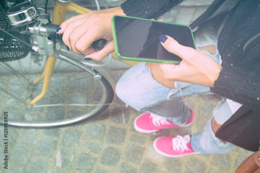 Girl using cellphone alongside with her bicycle.
