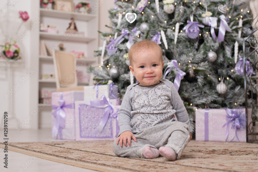 The baby girl is sitting next to the Christmas tree and boxes with gifts The baby girl is sitting next to the Christmas tree and boxes with gifts