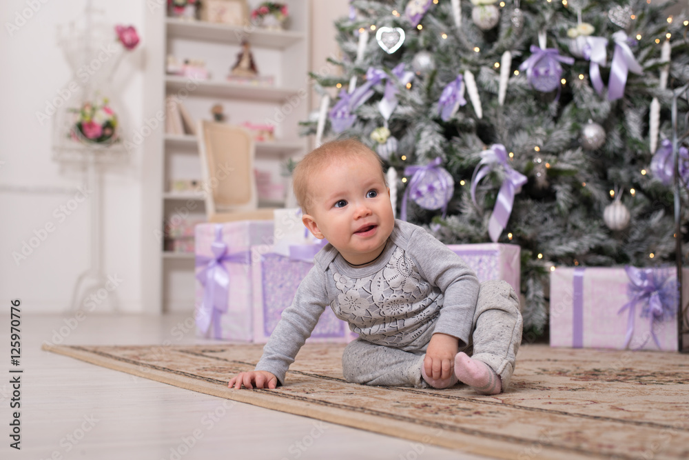 The baby girl is sitting next to the Christmas tree and boxes with gifts The baby girl is sitting next to the Christmas tree and boxes with gifts