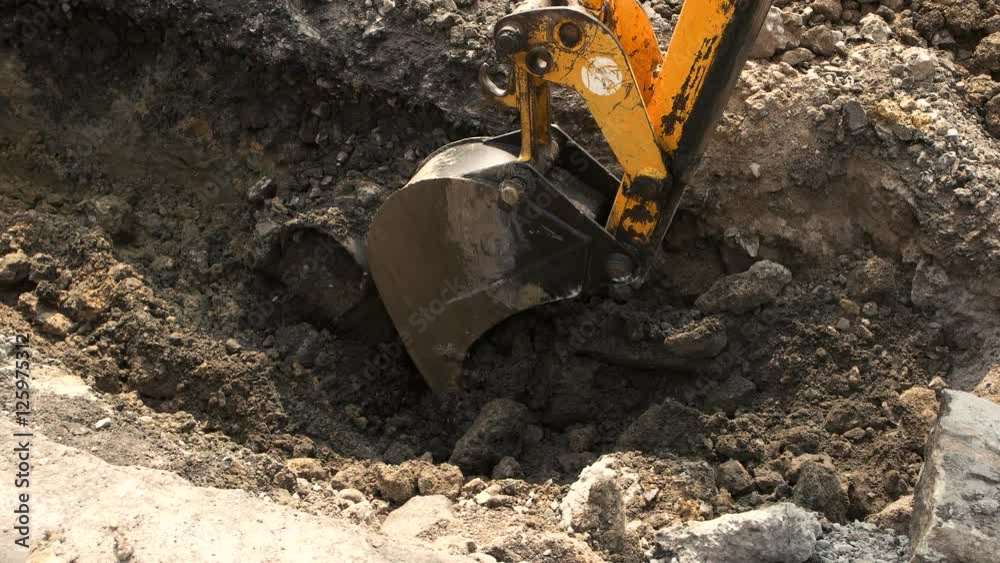 Bucket of excavator in motion. Machine digs a pit. Metal and dirt. Building a trench for cables. Bucket of excavator in motion. Machine digs a pit. Metal and dirt. Building a trench for cables.