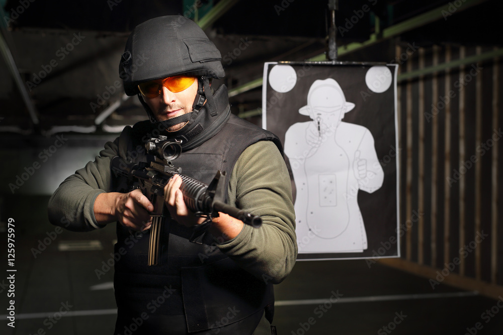 Obraz premium Żołnierz strzela z karabinu na strzelnicy. Mężczyzna w kamizelce kuloodpornej strzela na strzelnicy z karabinu