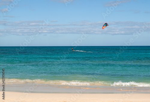 Unknown kitesurfer surfing on a flat azure water of Atlantic ocean in Corralejo, Fuerteventura, Canary islands, Spain