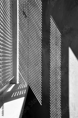 Geometric black and white composition. The plane of the plaster wall with a structural graphic shadow falling from the blinds. Vertical view.