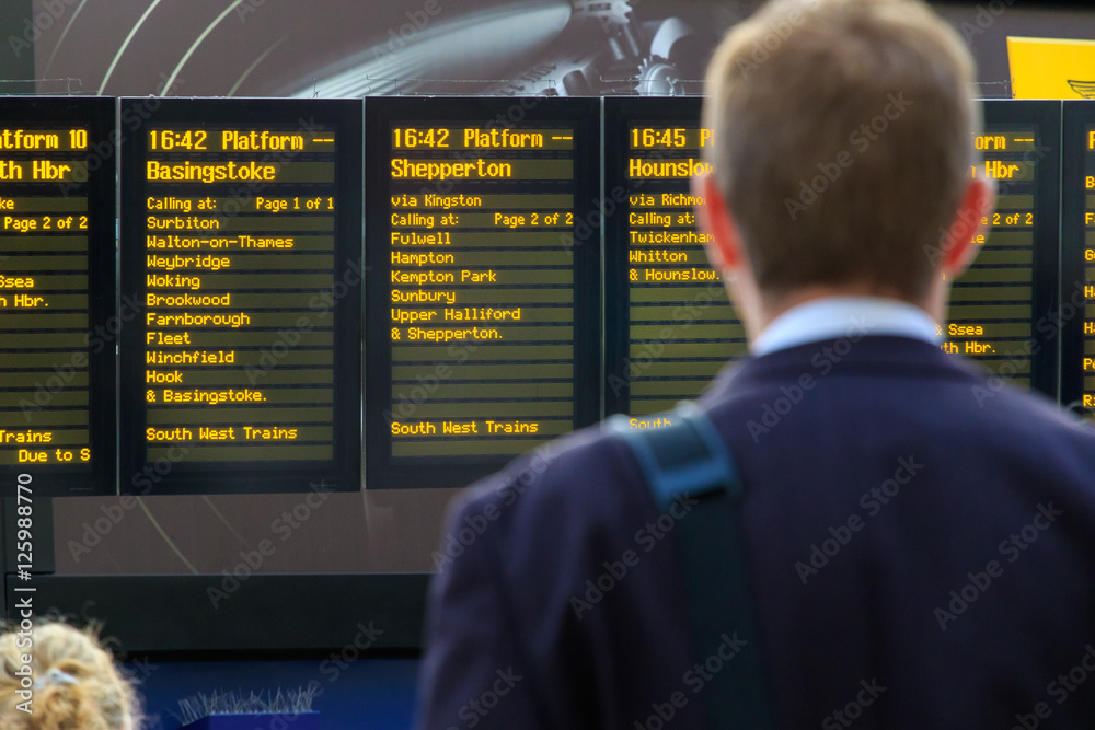 Obraz premium Dojeżdżający do pracy sprawdzający cyfrowy rozkład jazdy na stacji kolejowej
