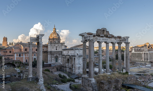 Roman buildings and ruins, in Rome, set against a deep blue sky with large white clouds, tinged with yellow and orange