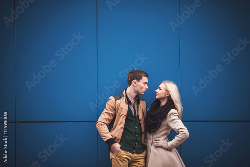 Young couple, boy and girl looking at ech other on blue wall background, a lot of empty space