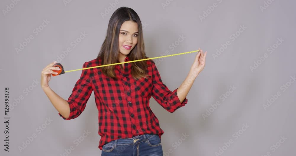 Female constructor worker with measure tape. She joking and playing around having fun. Wearing red checkered shirt and jeans. Isolated on gray background Female constructor worker with measure tape. She joking and playing around having fun. Wearing red checkered shirt and jeans. Isolated on gray background