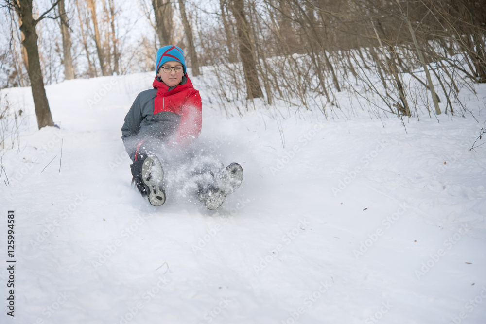  Teenage boy in glasses quickly moves down on a sled with snow slides,.motion blur