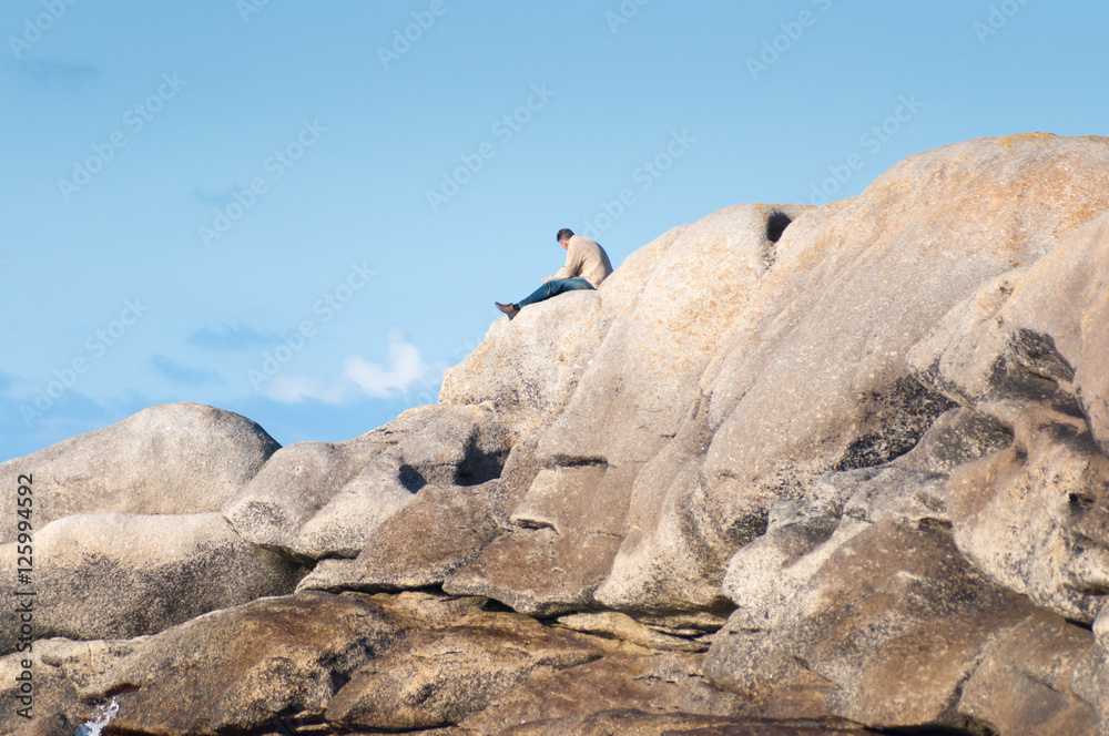 ein Mann sitzt auf einem Felsen und schaut entspannt auf das Meer bei Meneham, Brignogan, Bretagne, Frankreich