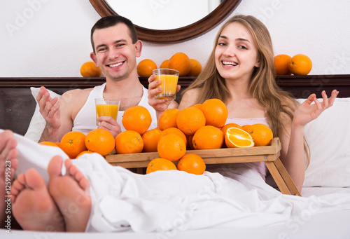 man and girlfriend drinking squeezed orange juice in bed