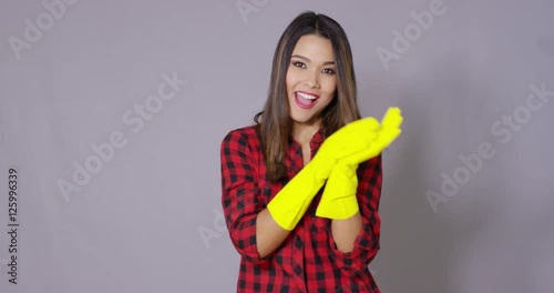 Attractive housewife holding up gloved hands in colorful yellow rubber gloves with a wry smile as she prepares to do the housework